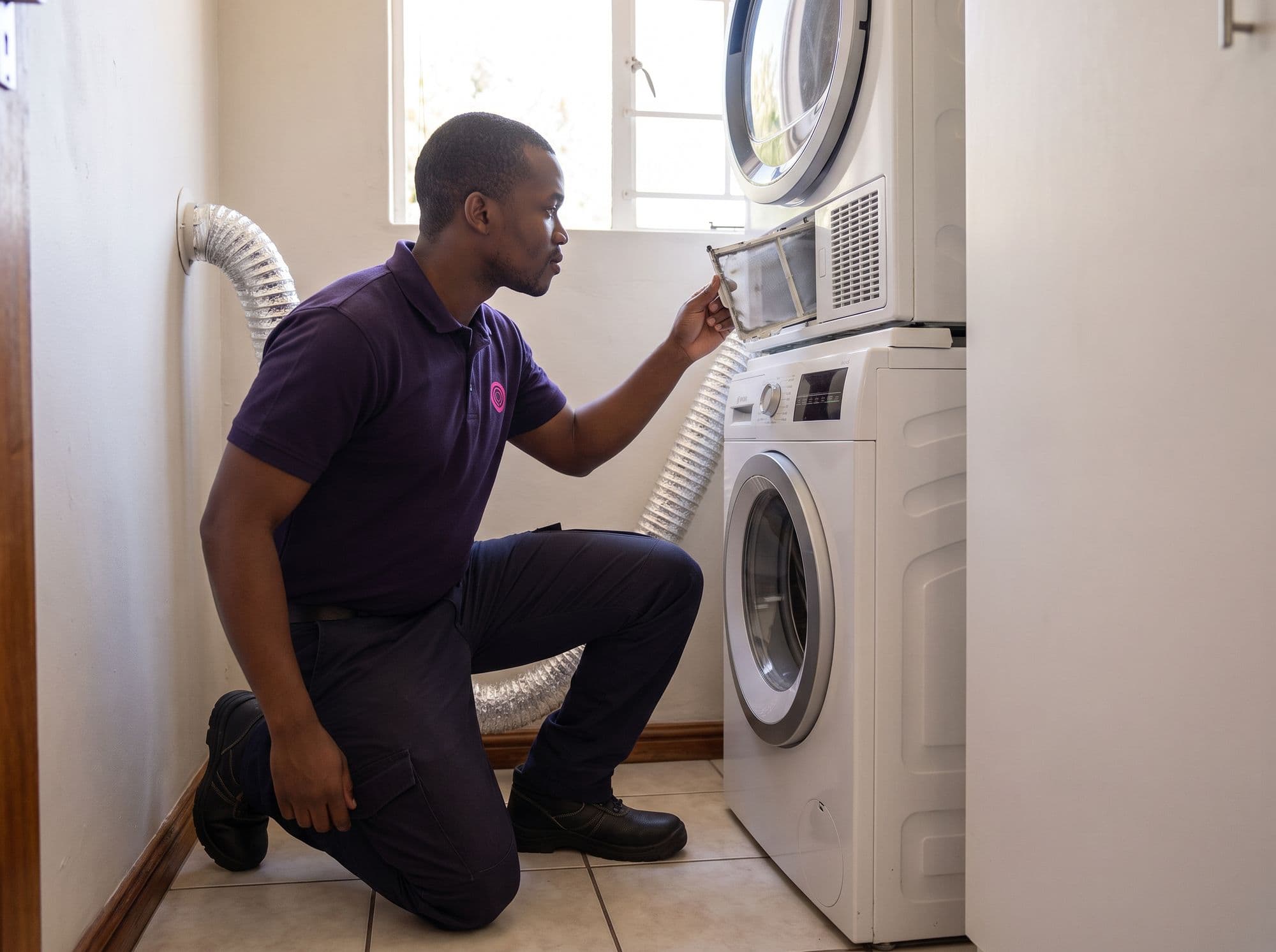 A technician pulls the lint filter from a tumble dryer stacked on a washing machine